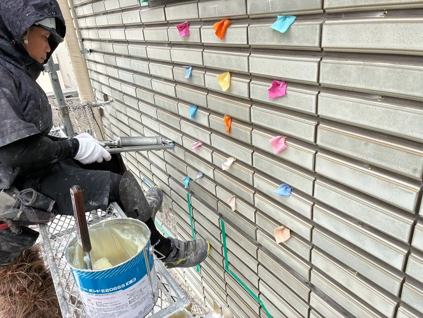 作業員が足場の上でタイル外壁にエポキシ樹脂を注入している様子